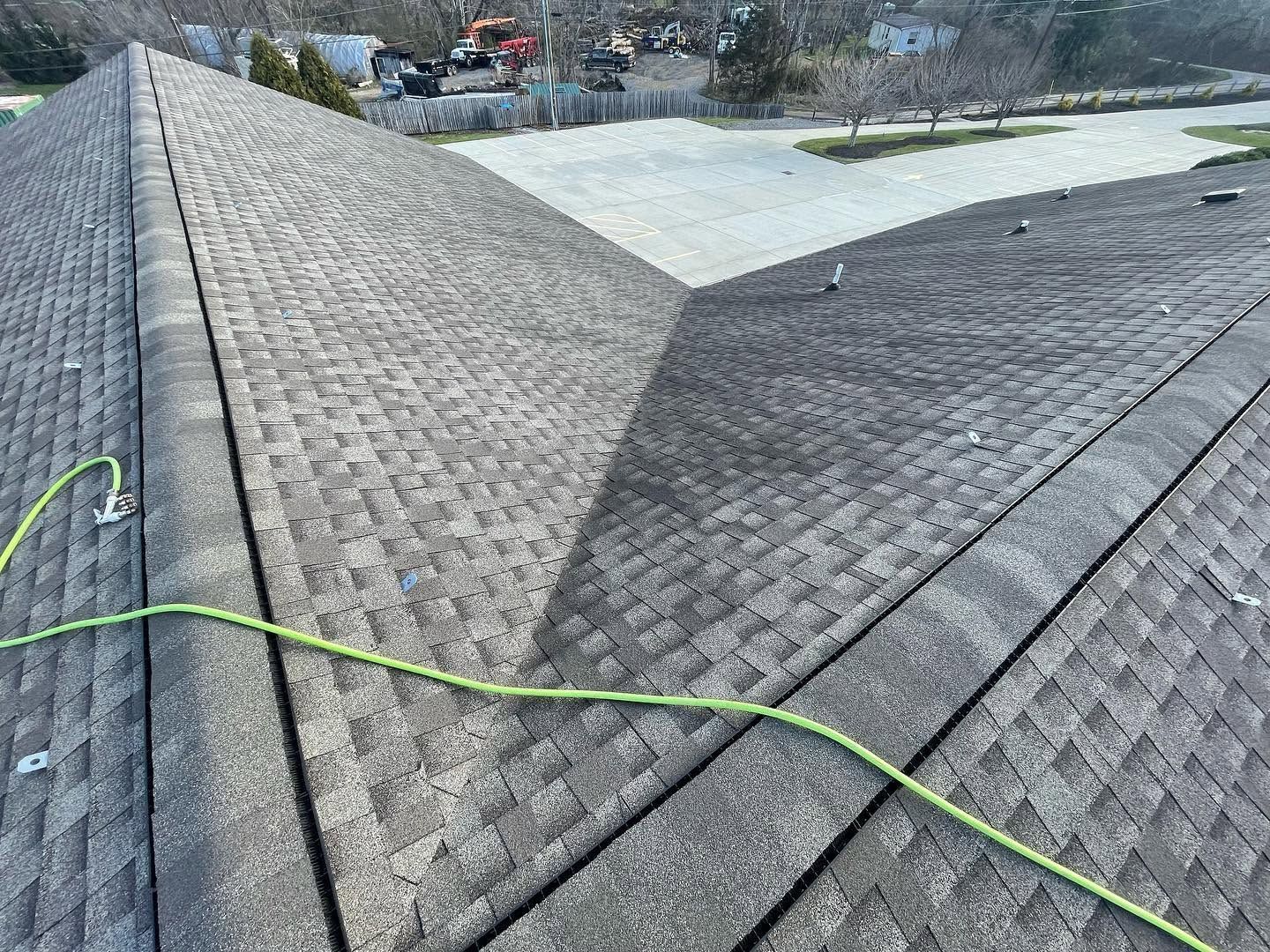 Roof shingles on a house, with a green rope or hose running across the roof ridge.