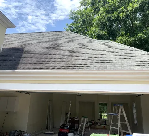 Open garage with ladders and tools under a gray shingled roof