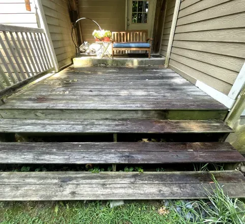 Weathered wooden porch steps leading to a deck beside beige siding and a white railing.