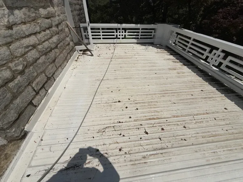 Sunlit white wooden deck beside a stone wall and white railing, with a person’s shadow in the foreground