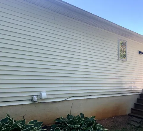 White house siding with foundation vents and shrubs, viewed from the side near steps