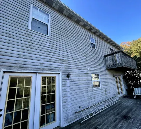 Back of a white house with French doors, deck, balcony, and ladder leaning against the siding