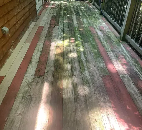 Weathered wooden deck with faded red and white planks beside a railing, dappled with sunlight and shadows
