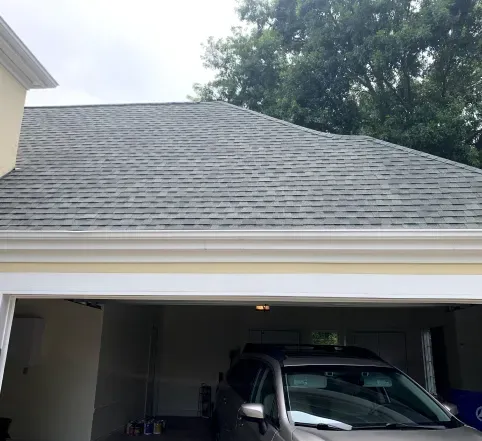 Gray shingled suburban house with an open garage and a dark SUV parked inside