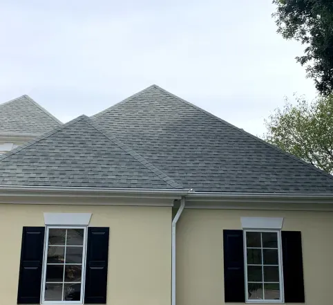 Two-story beige house with a gray shingle roof and white-trimmed windows with black shutters