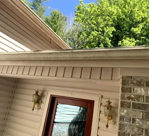 House eaves and brick entry with two brass lanterns beside a red front door under green trees
