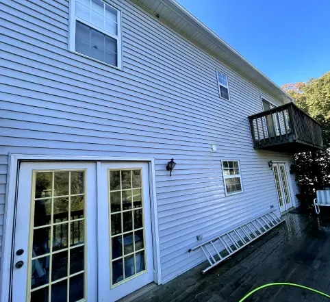White-sided house exterior with French doors, second-story deck, and ladder leaning against the wall.