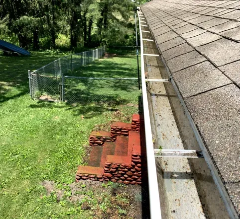 Backyard with wire fence, stacked bricks, and a roof gutter along a shingled roofline