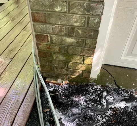 Soapy water pooling beside a brick wall and white door next to a wooden deck