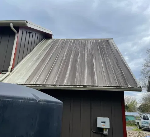 Weathered metal roof on a dark building, with a cloudy sky and a black tank in the foreground.