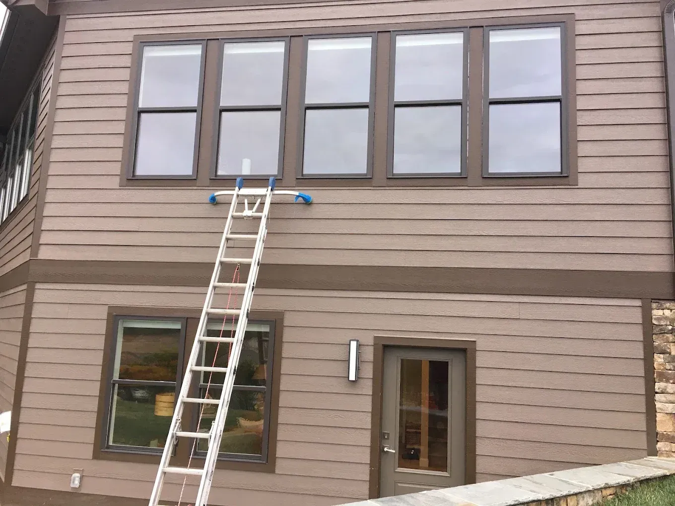 Ladder leaning against a two-story tan building with large windows and a door below.