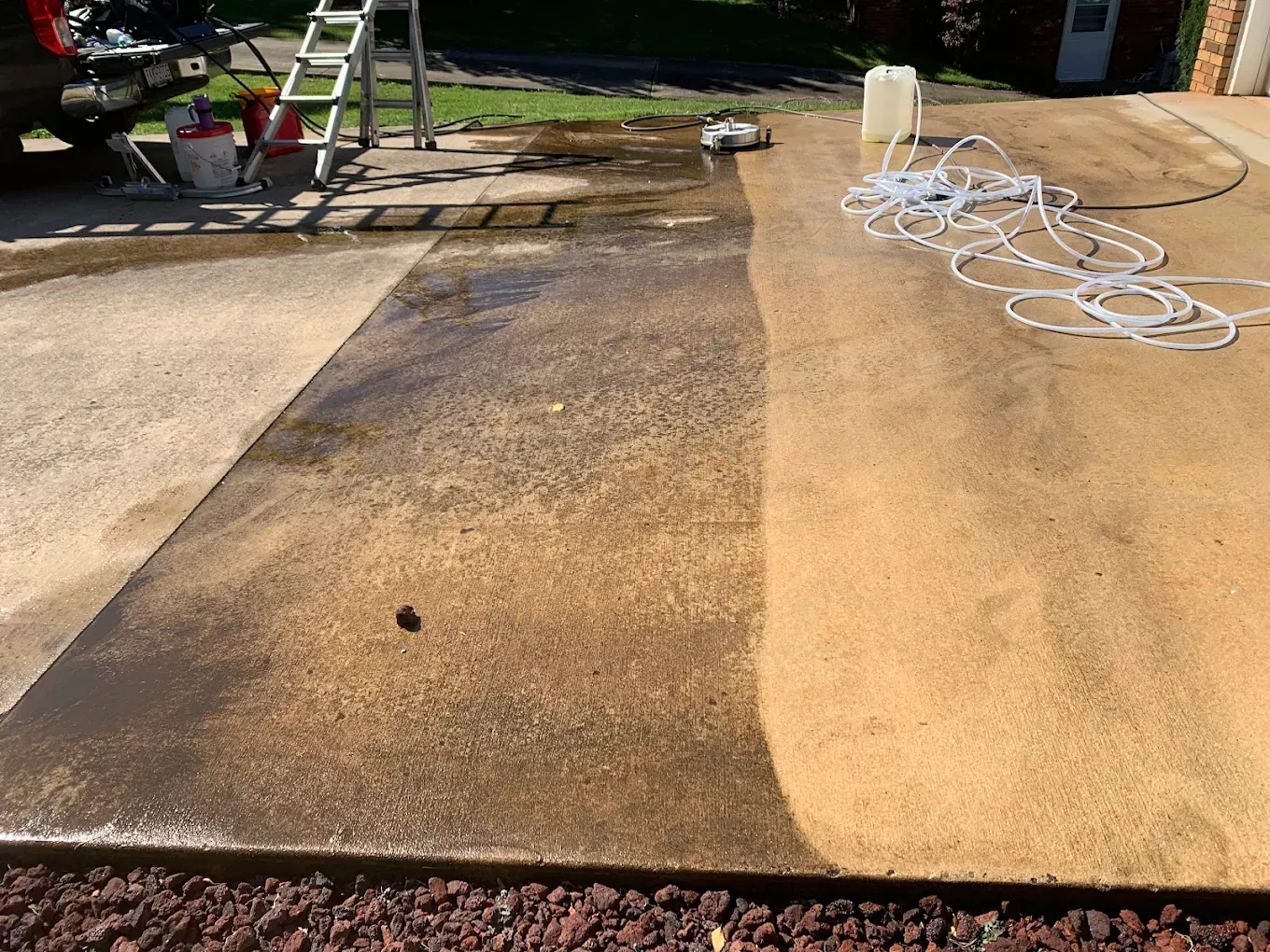 Outdoor patio with a wet, dark-stained concrete strip, ladder in the background, and coiled hose on the right.