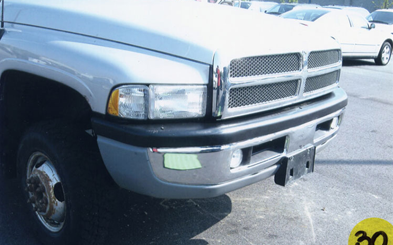 Silver Dodge Ram truck's front with chrome grill, headlights, and bumper in a parking lot.