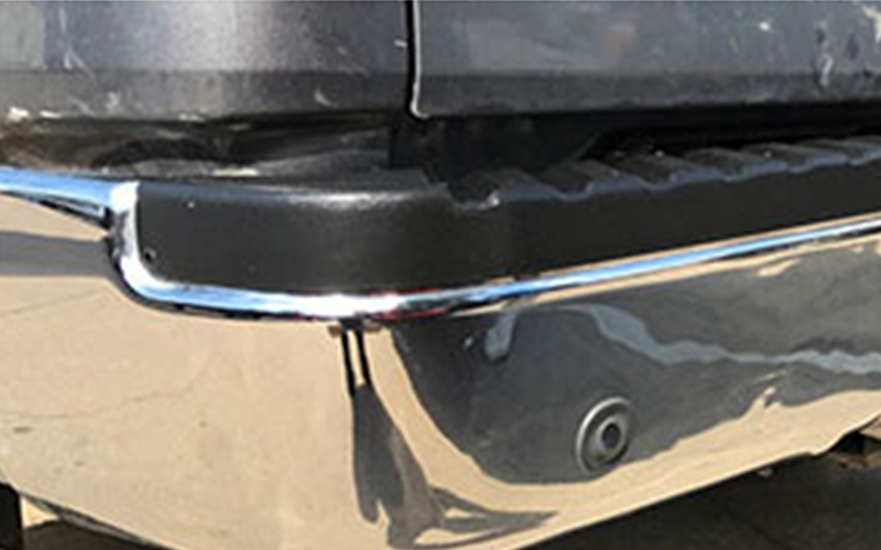 Rear bumper of a gray pickup truck, with a chrome trim and a parking sensor.