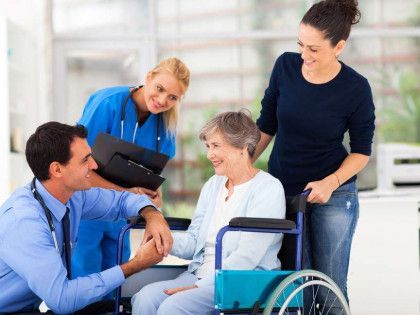 Four caregivers smiling and talking with an older woman in a wheelchair in a bright clinic
