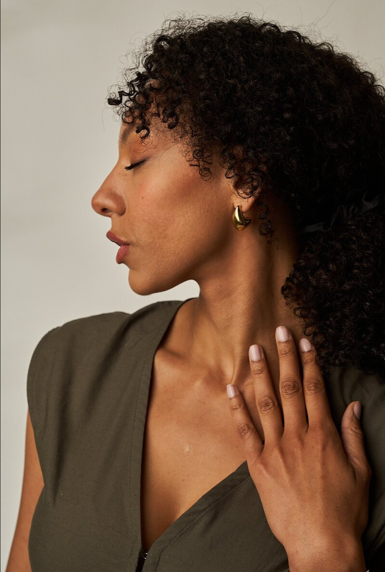 Frau mit dunklem Bob, die nach oben blickt, trägt ein beigefarbenes Oberteil vor einem cremefarbenen Hintergrund.