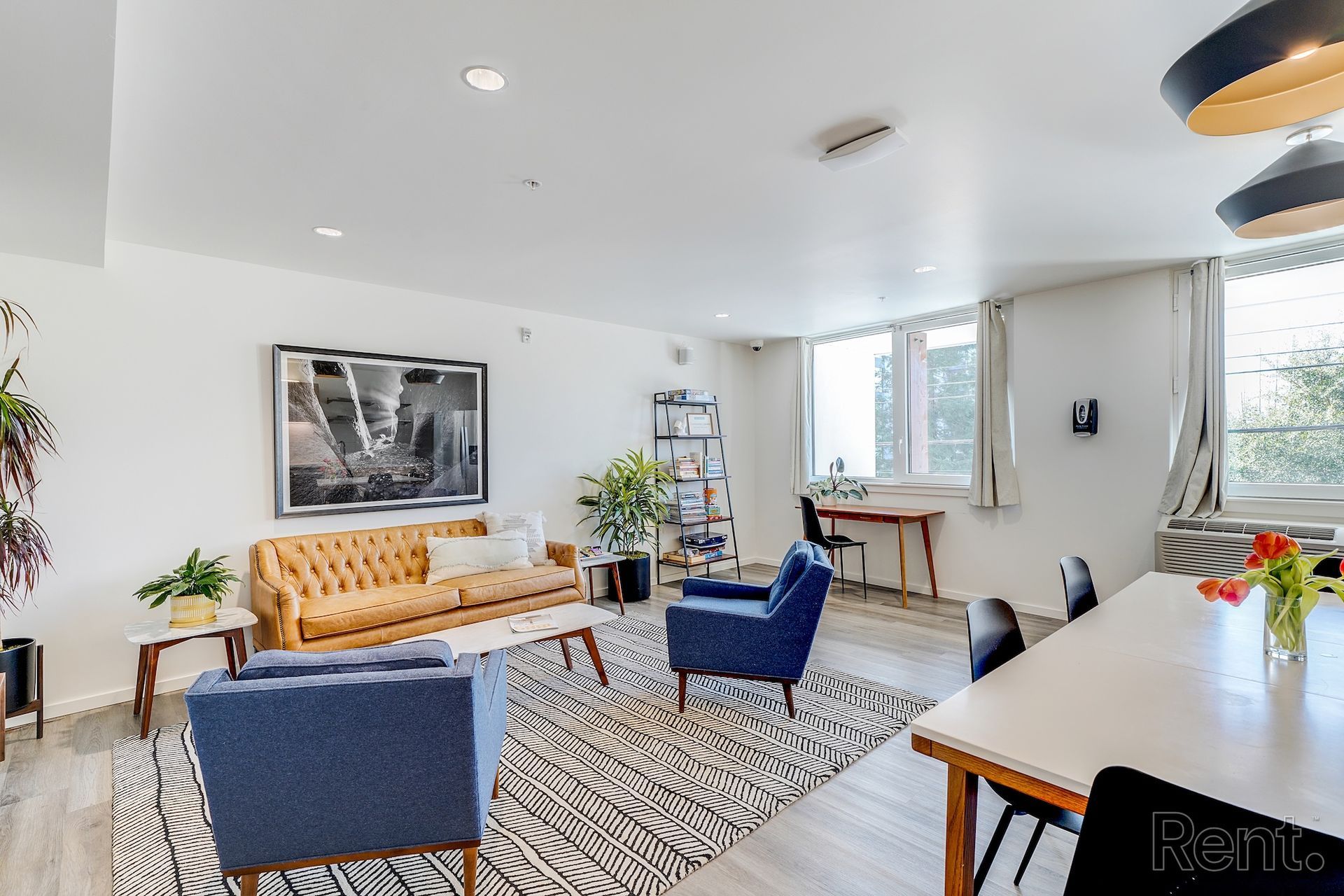 Bright living room with mustard sofa, blue chairs, patterned rug, and dining table near windows