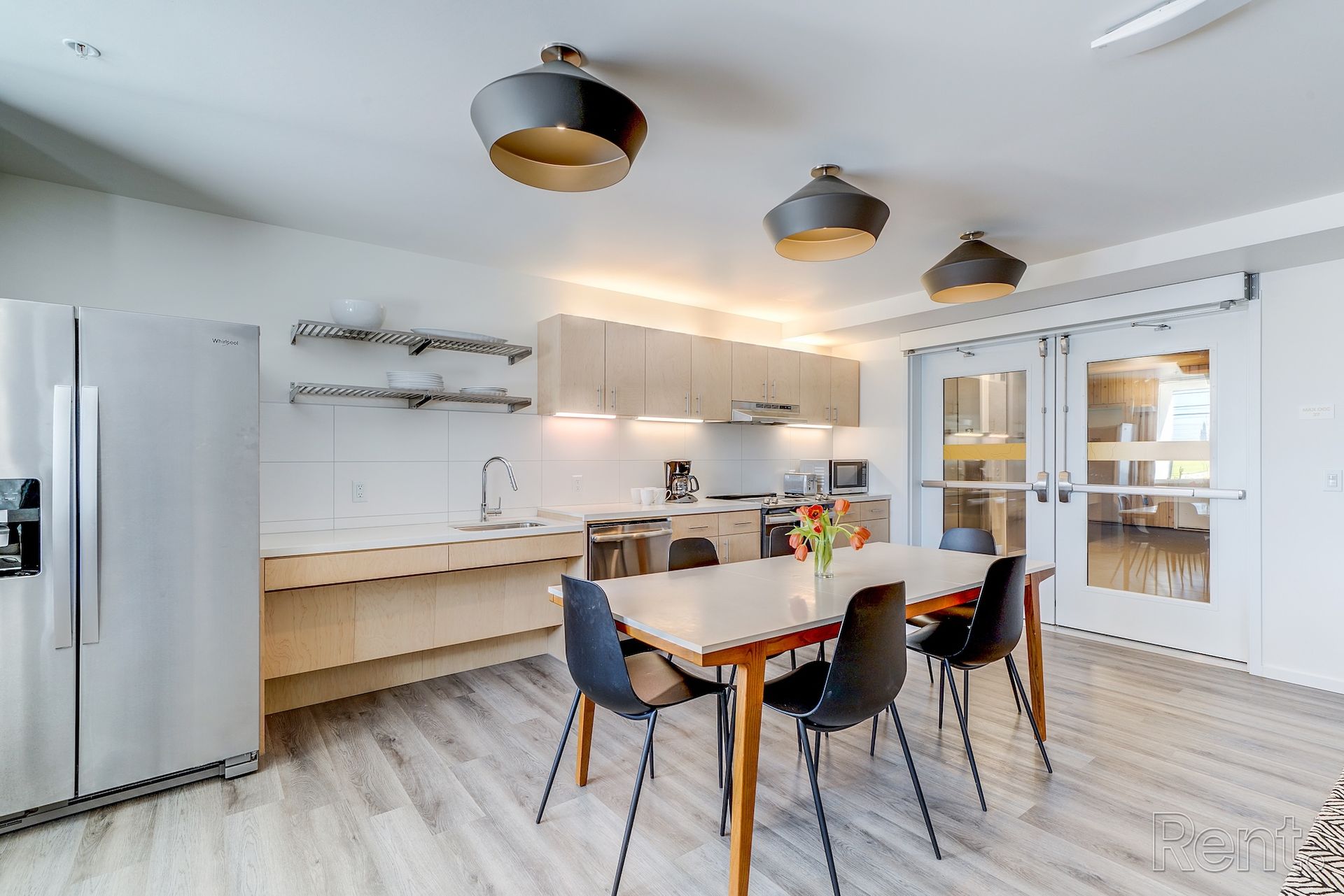 Modern white kitchen and dining area with stainless steel fridge, light wood table, and black chairs