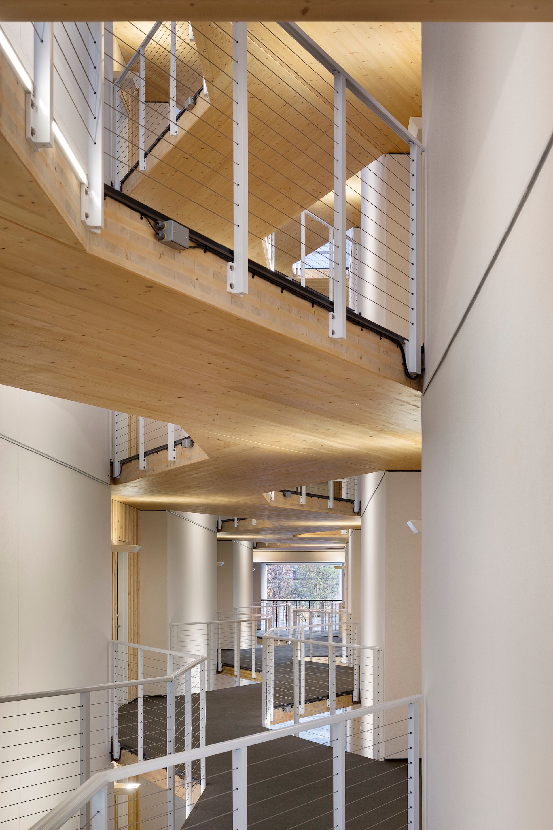 Modern stairwell with white railings, wooden beams, and a central open atrium.