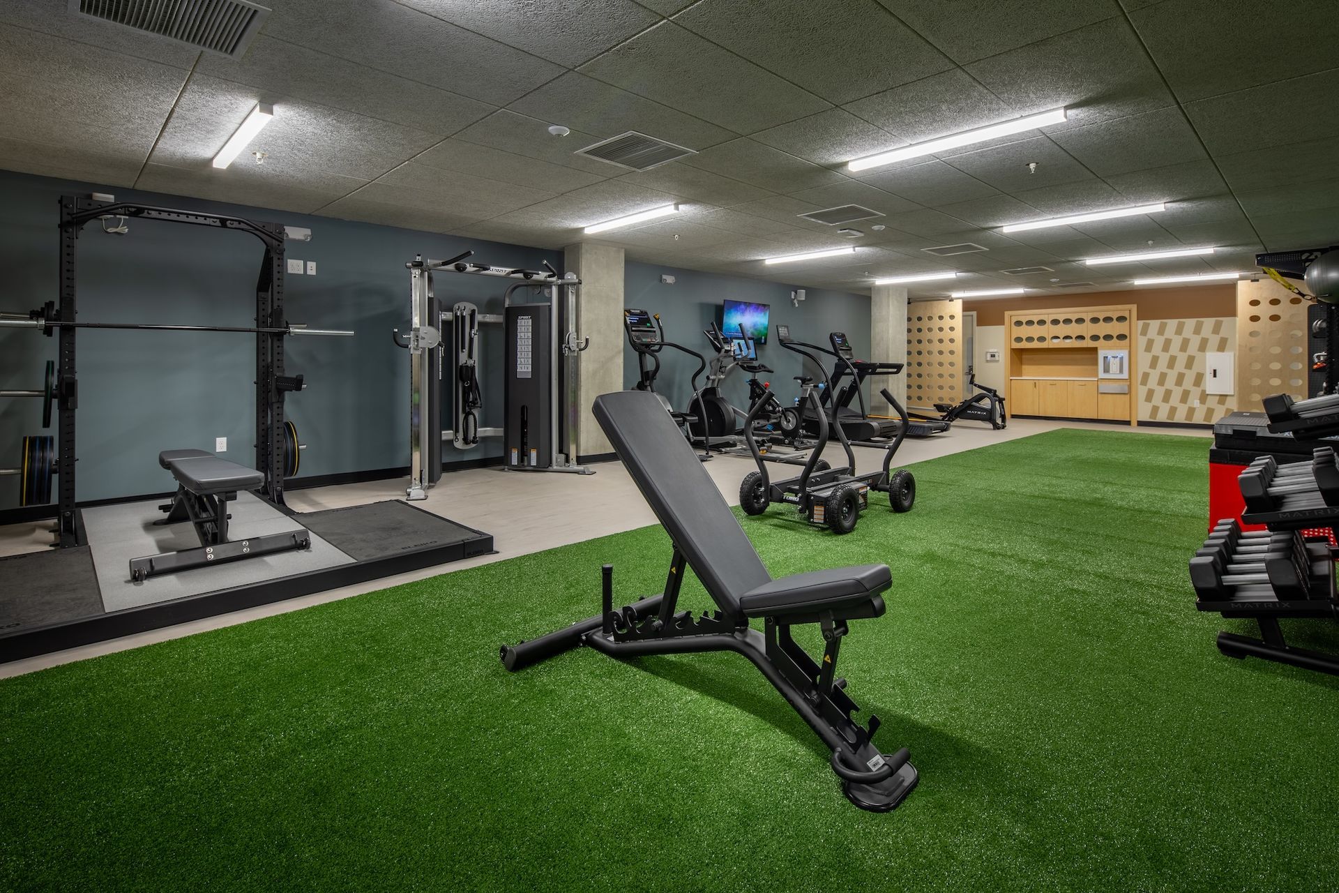 Modern gym with turf, weight bench, cable machine, and exercise bikes
