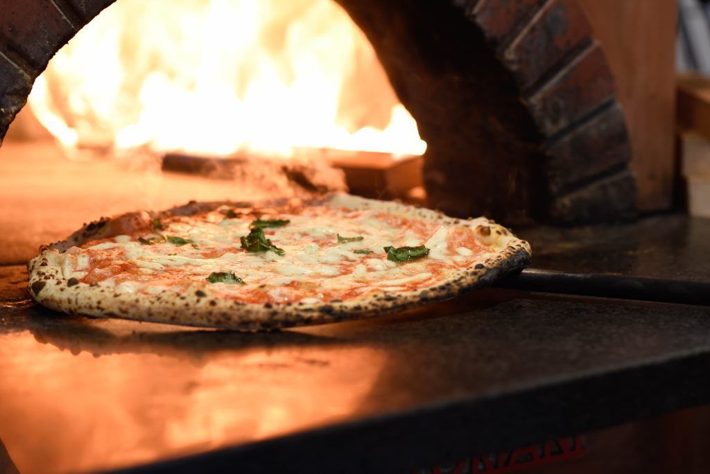 Pizza cotta in un forno a legna con fiamme sullo sfondo.