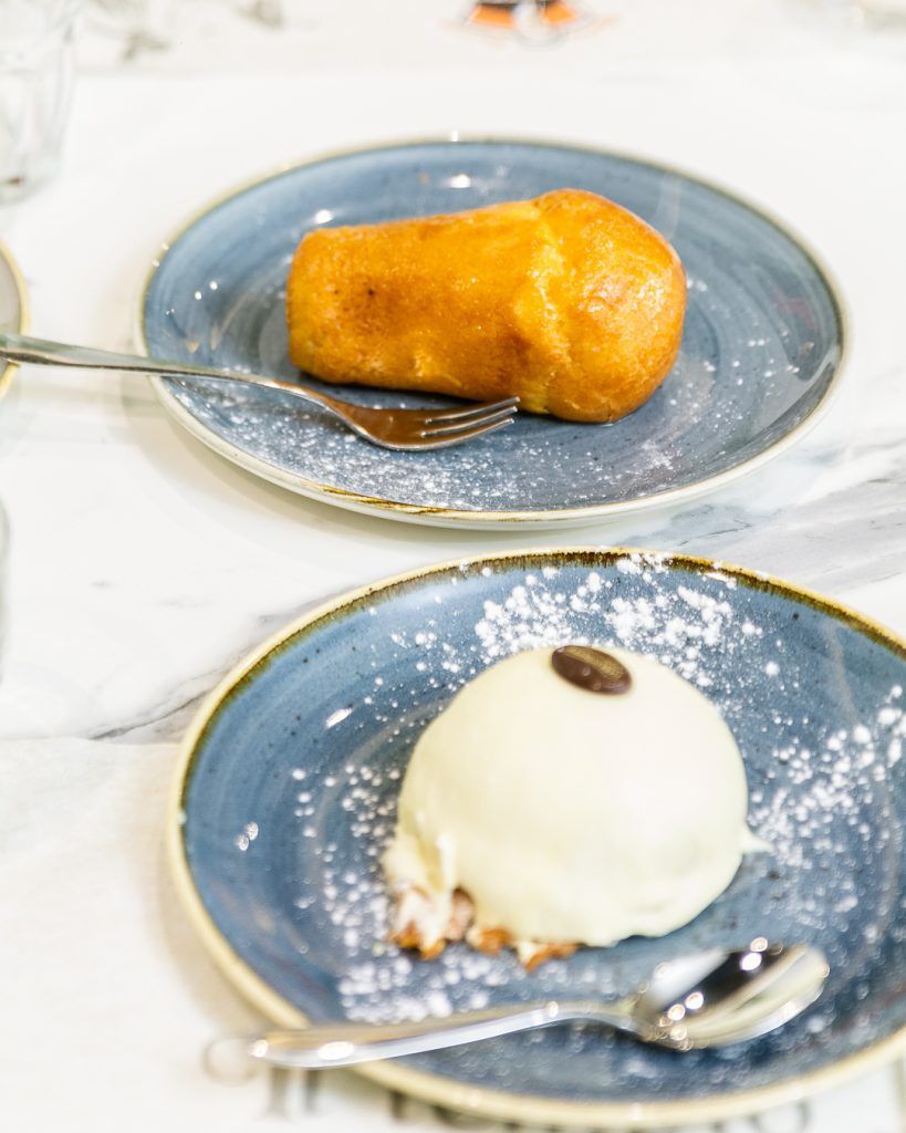 Due pasticcini su piatti blu: uno è una brioche dorata, l'altro è una cupola glassata di bianco con un chicco di caffè.