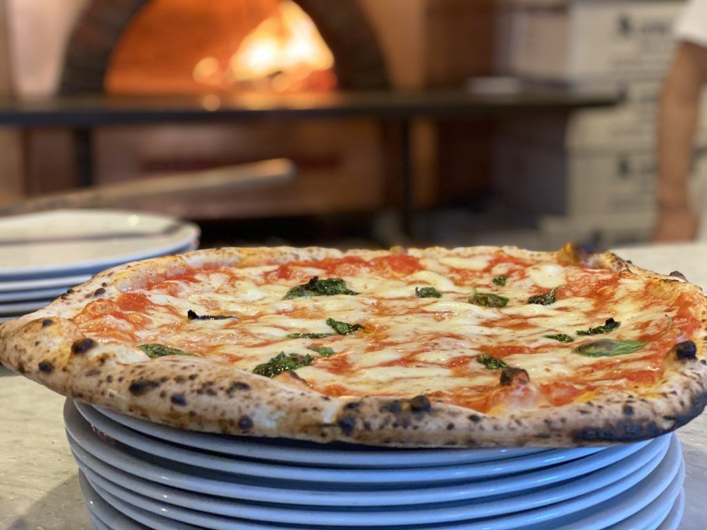 Pizza su una pila di piatti, con un forno a legna sullo sfondo.