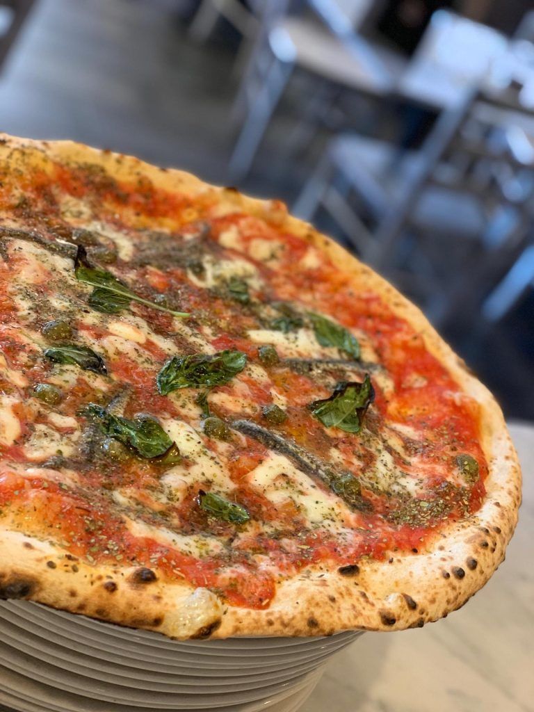Pizza con salsa di pomodoro, basilico, acciughe, su una pila di piatti; sfondo sfocato del ristorante.