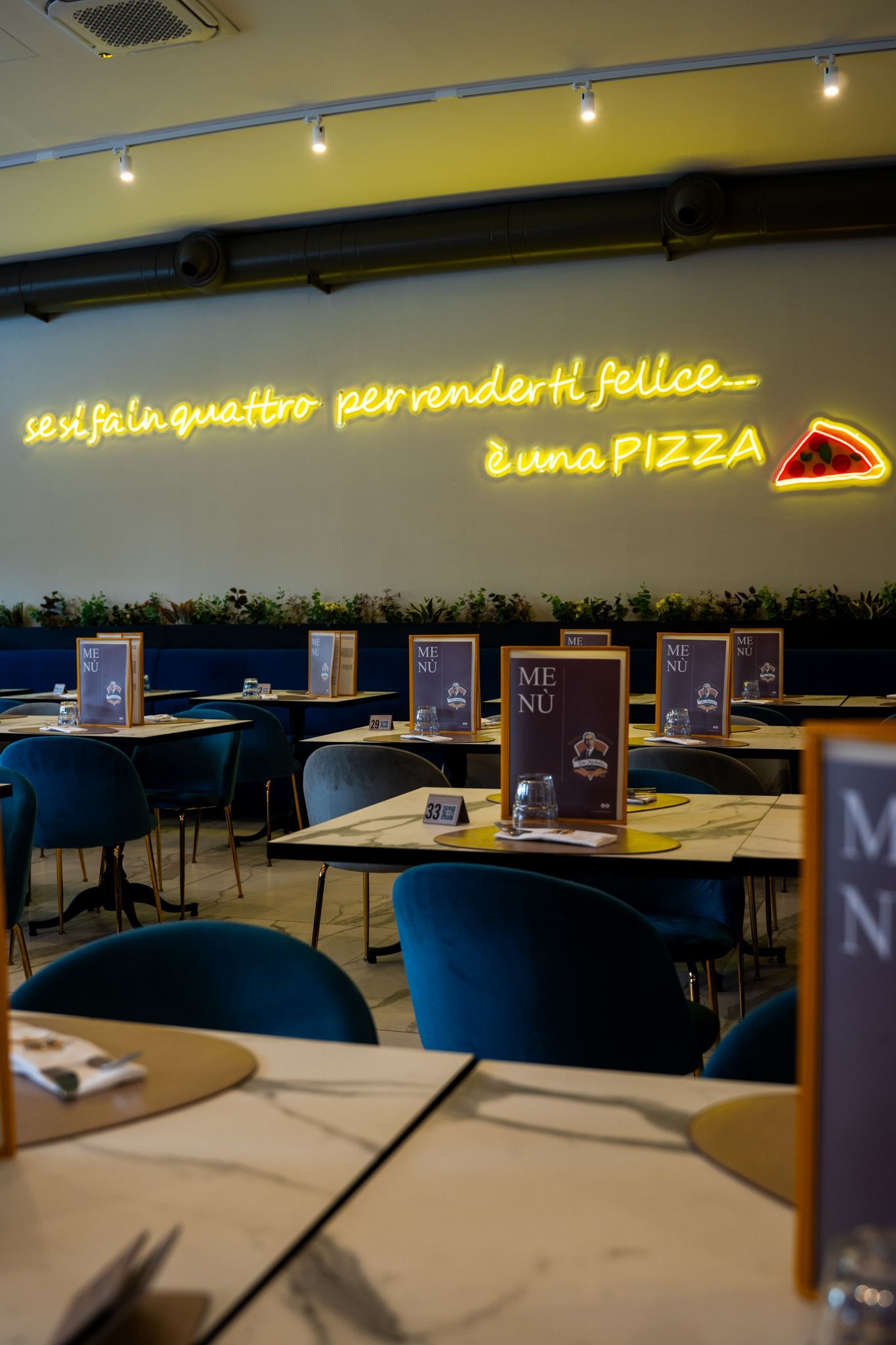 Interno del ristorante con tavoli, sedie blu e un'insegna al neon con la scritta 