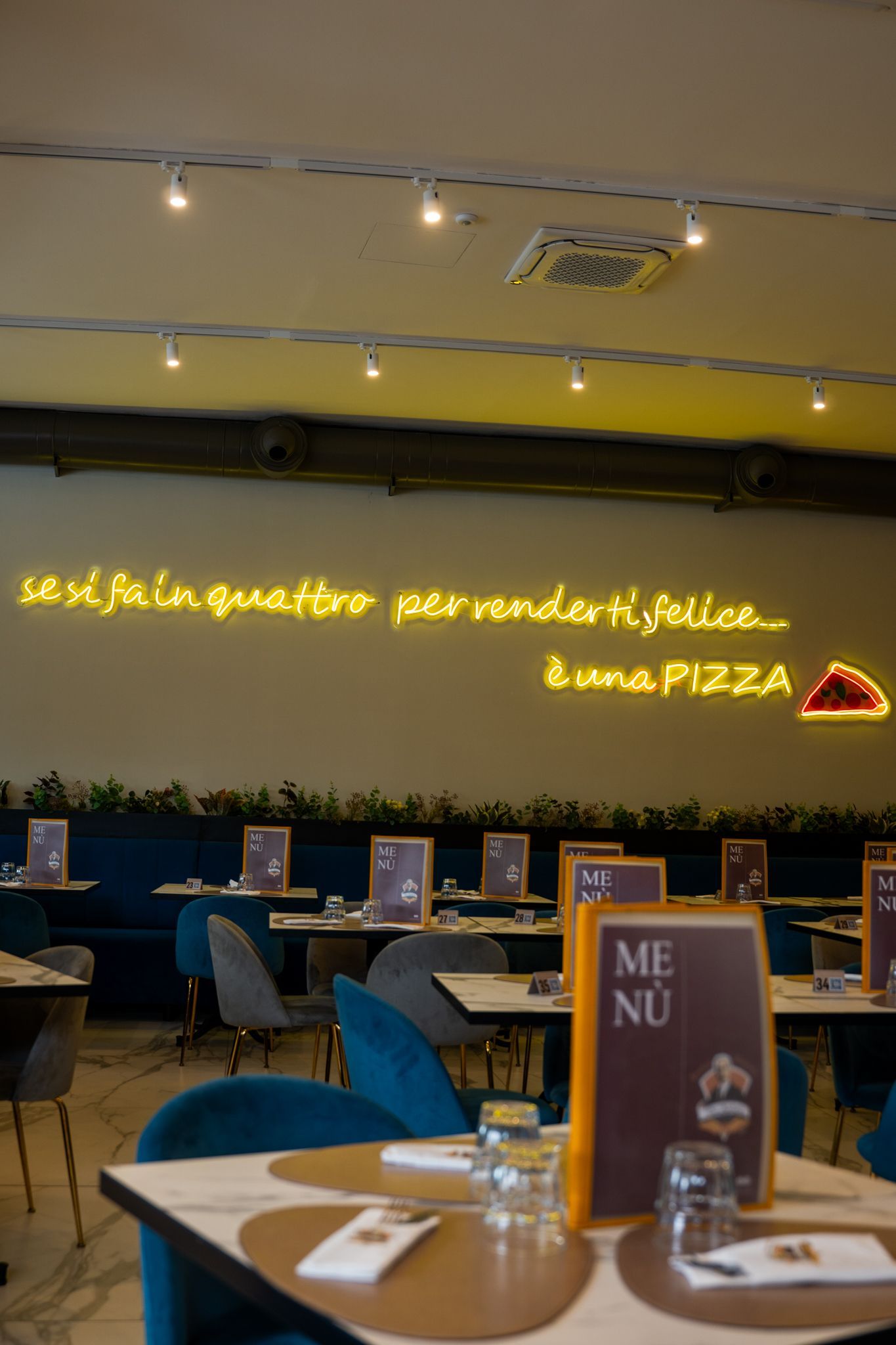 Interno del ristorante con tavoli, sedie blu e un'insegna al neon con la scritta