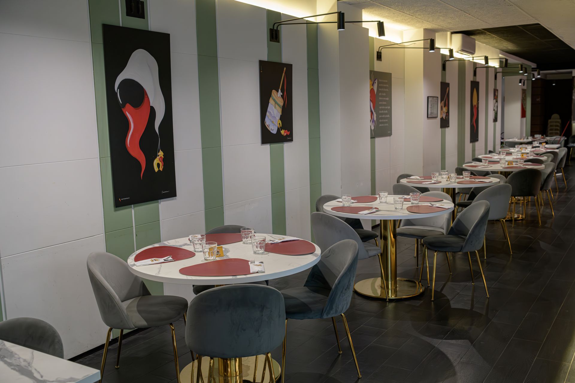 Interno del ristorante con tavoli rotondi, sedie, opere d'arte e pareti a strisce.
