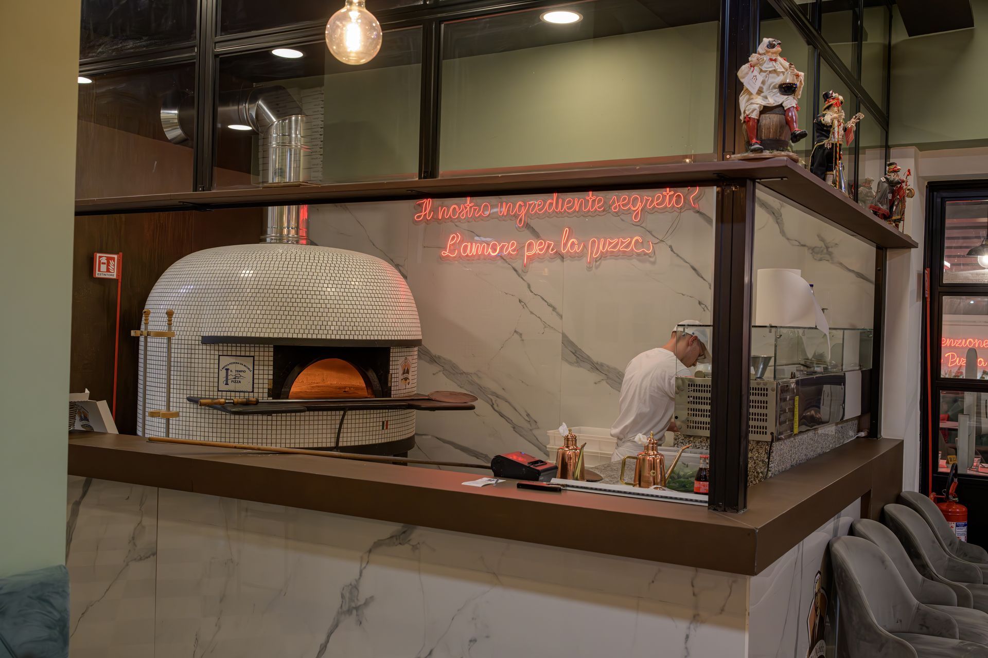 Forno per pizza e postazione di preparazione in un ristorante. Uno chef al lavoro, un'insegna al neon illuminata. Decorazioni in marmo e legno.