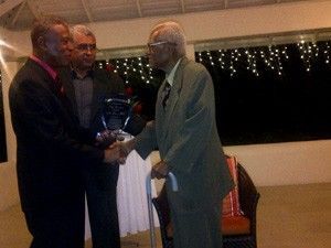 Three men shaking hands in a room with christmas lights in the background