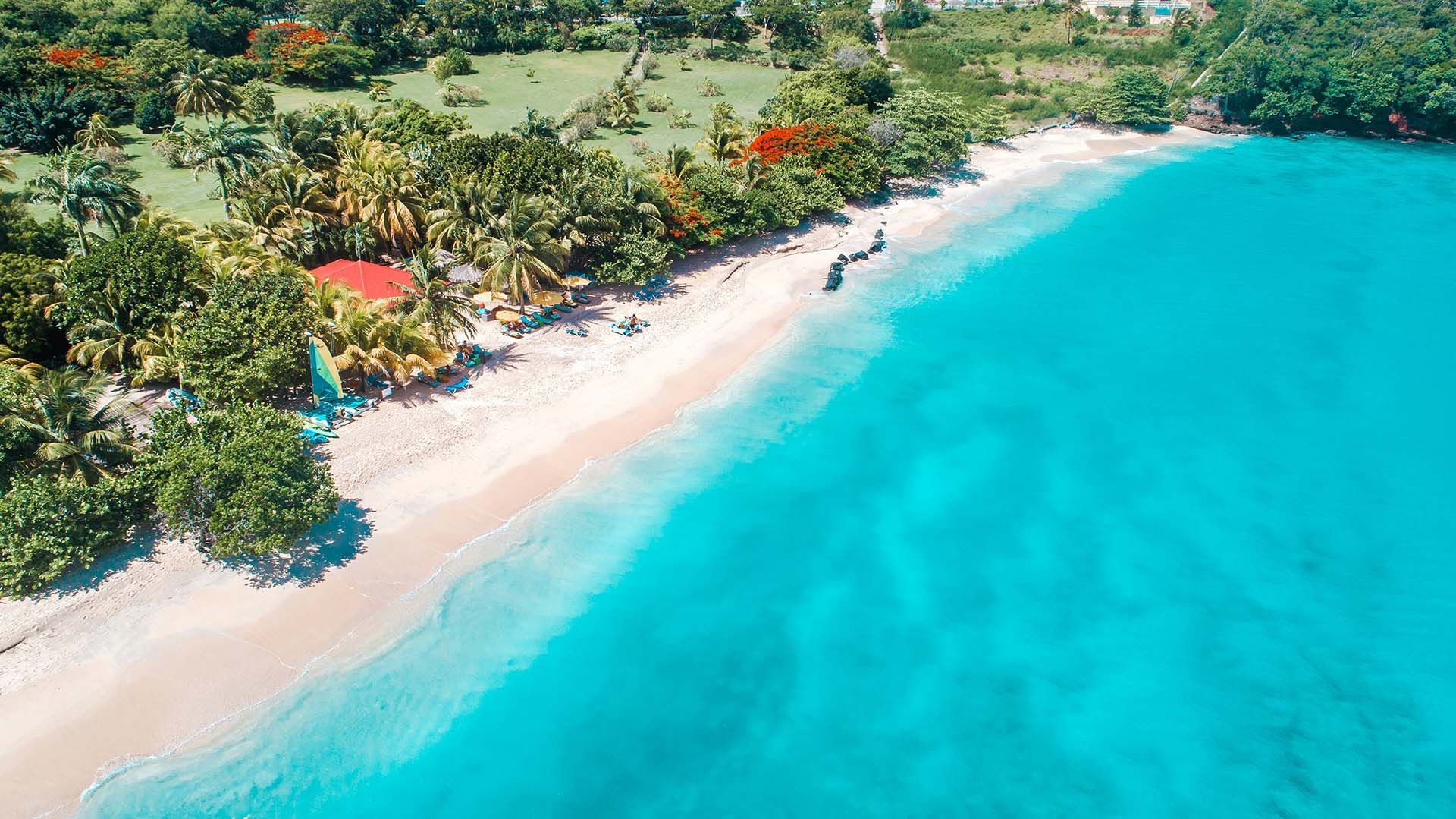 An aerial view of a tropical beach surrounded by trees and turquoise water.