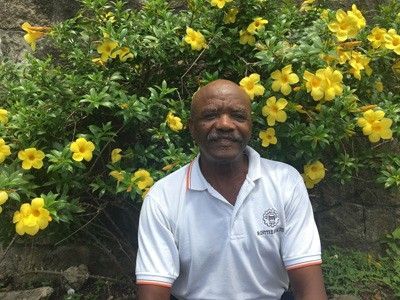 A man is sitting in front of a bush with yellow flowers.