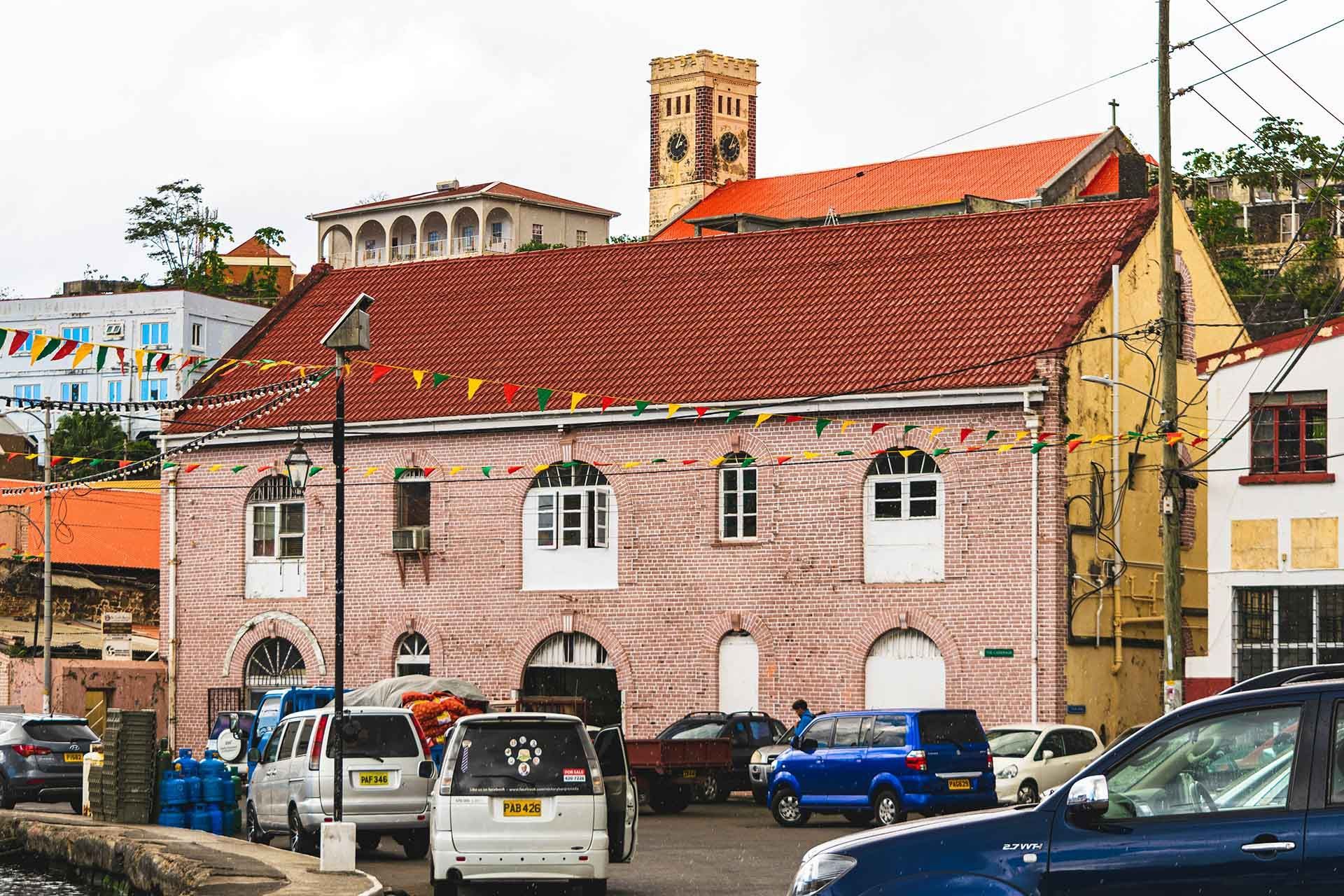A brick building with a red roof is surrounded by cars parked in front of it.