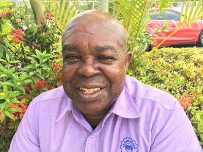 A man in a purple shirt is smiling in front of a bush.
