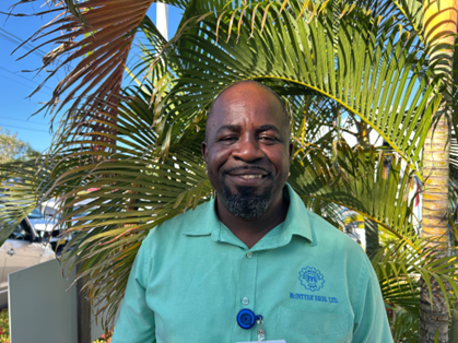 A man in a green shirt is standing in front of a palm tree.
