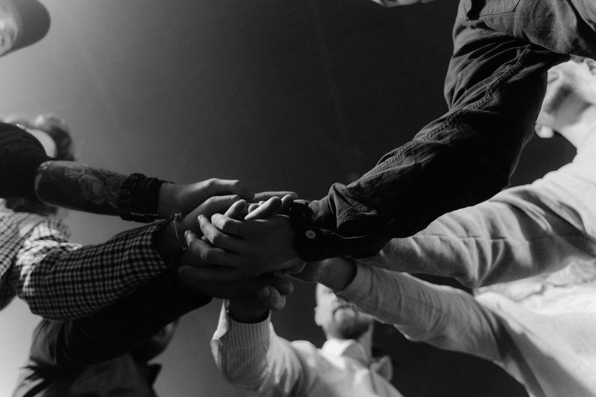 A group of people are putting their hands together in a black and white photo.
