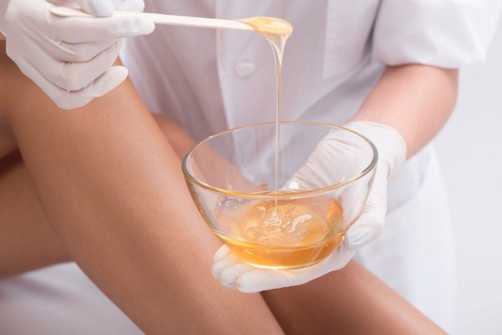 Person Wearing Gloves Waxing Leg With a Wooden Spatula, Wax in Glass Bowl — Eternal Radiance in Strathmore, VIC