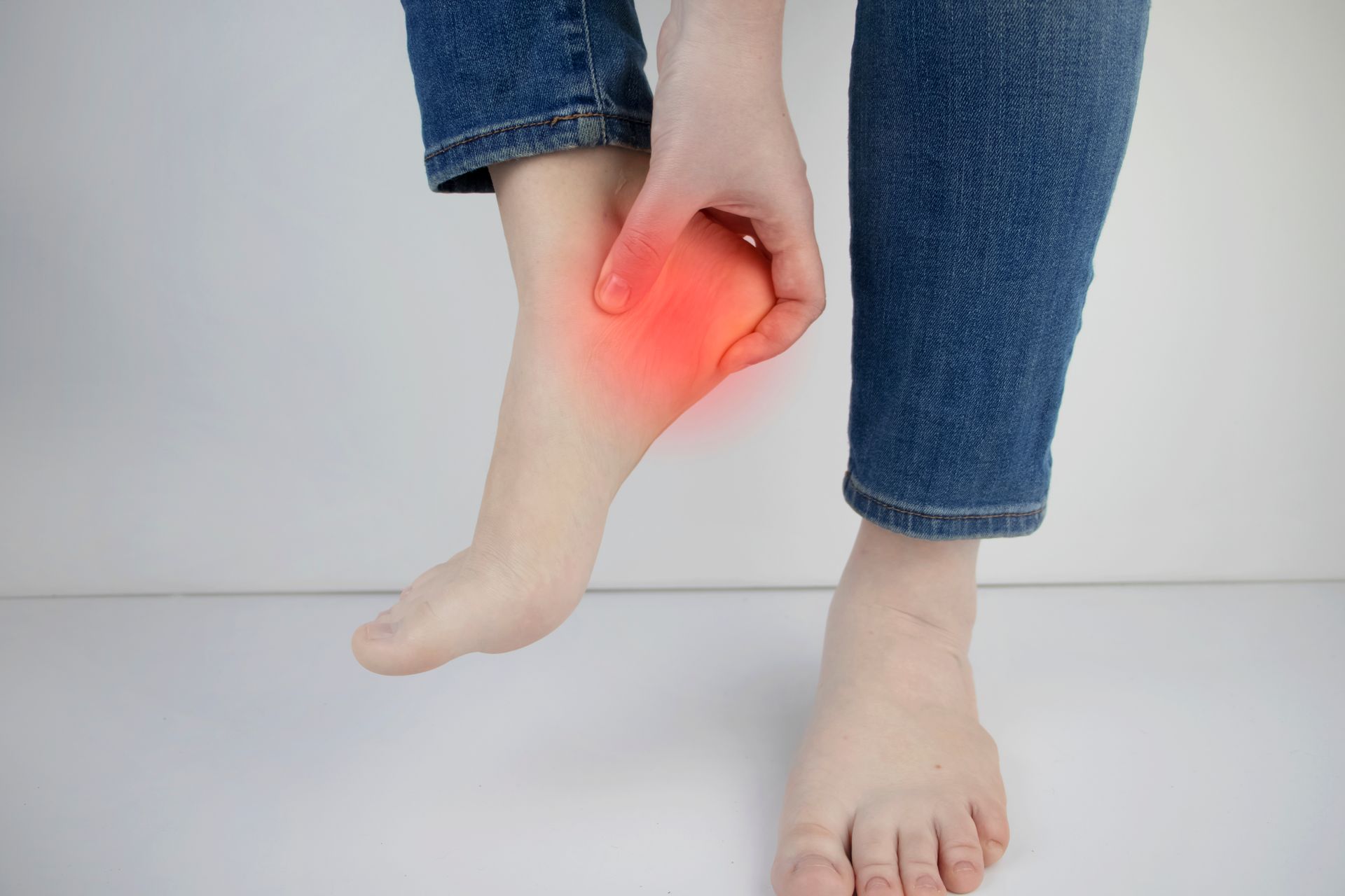 Person in jeans, holding their foot with red highlight indicating heel pain.
