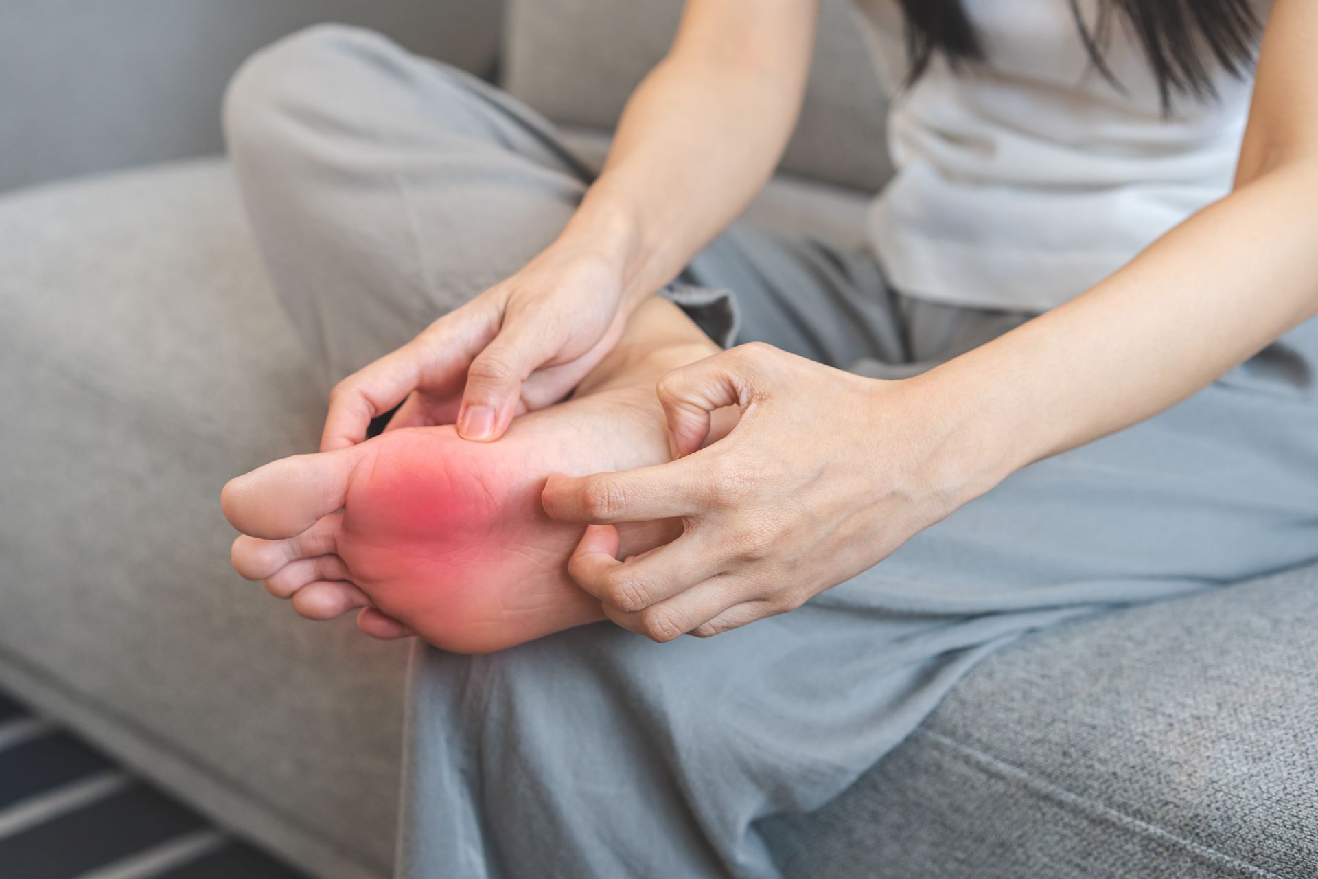 Person sitting on couch examining a red, inflamed foot.