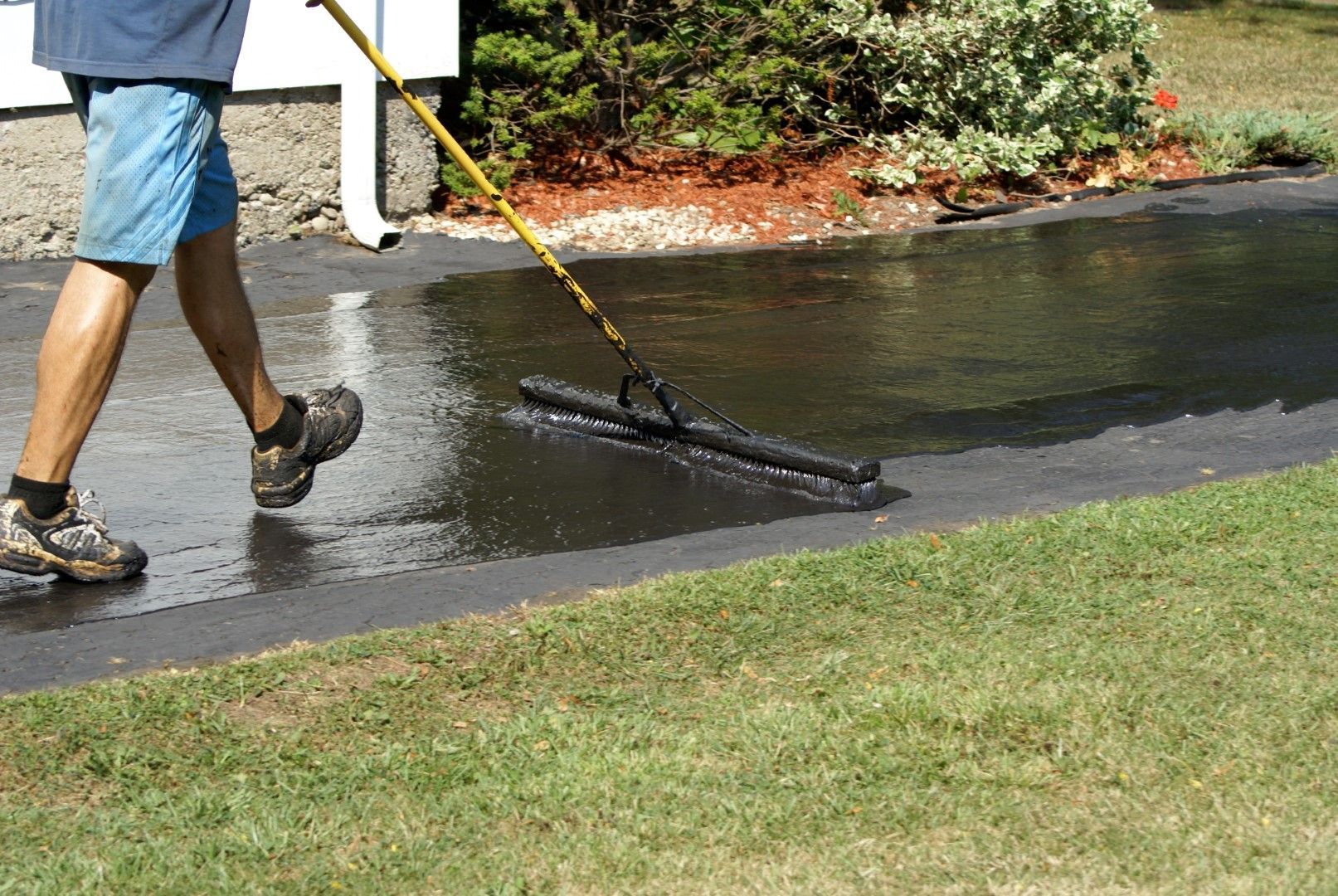 A man is walking down a wet driveway with a mop.