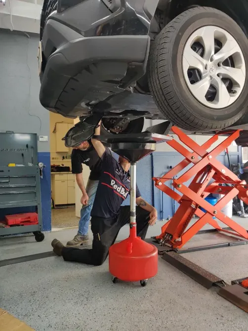 Mechanic inspecting the underside of a black SUV lifted on a red scissor jack in a garage