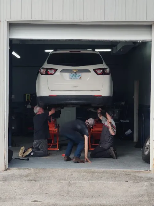 White SUV lifted in a garage while mechanics work underneath