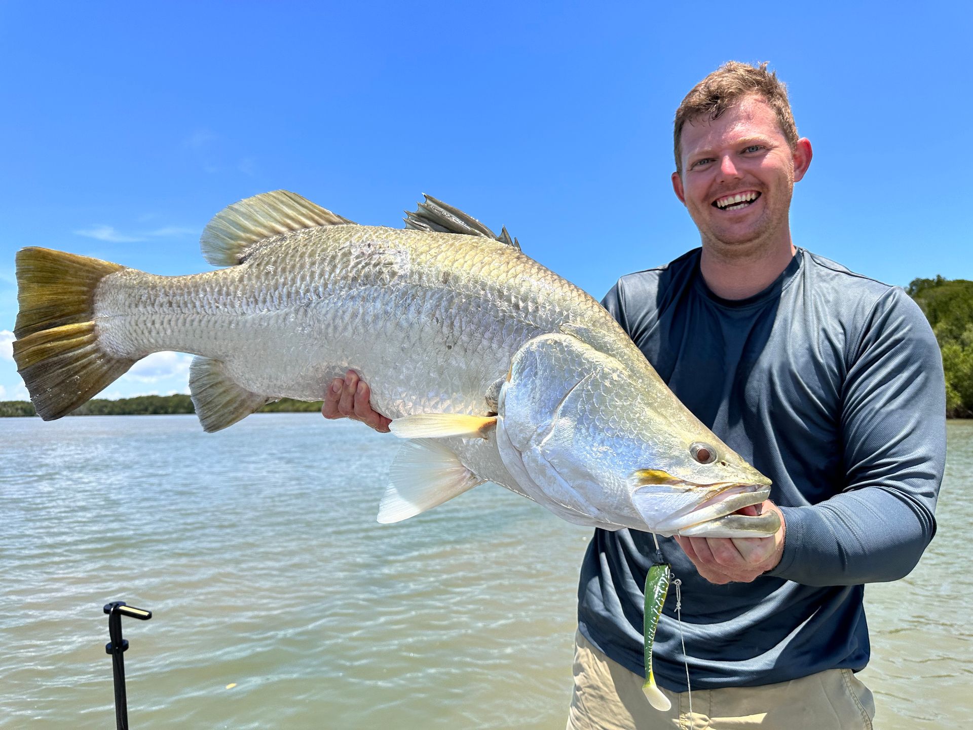A Man Is Holding A Large Fish In His Hands In Front Of A Body Of Water — Territory Barra Sportfishing In Zuccoli, NT