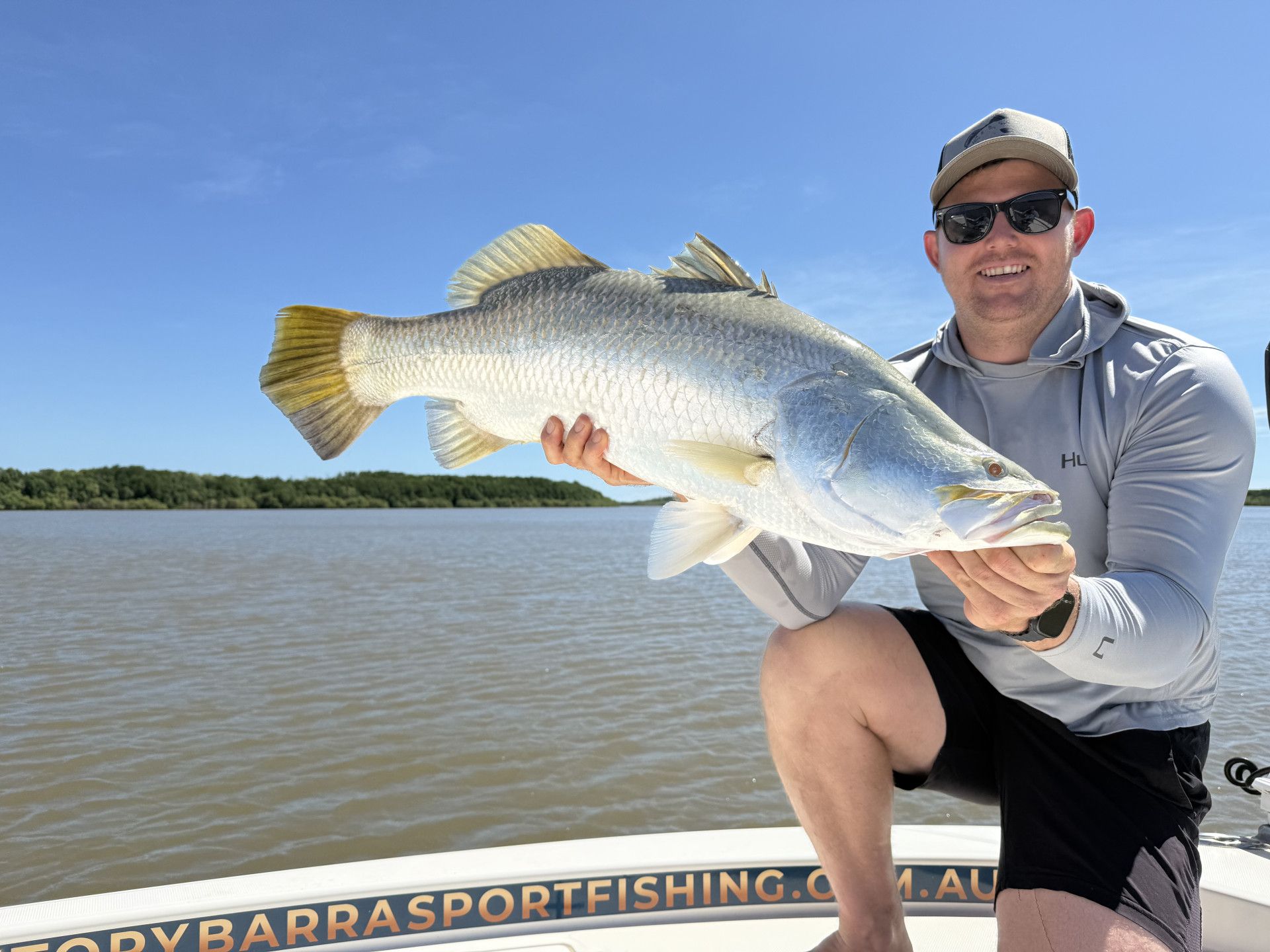A Man Is Holding A Large Fish In His Hands On A Boat — Territory Barra Sportfishing In Zuccoli, NT