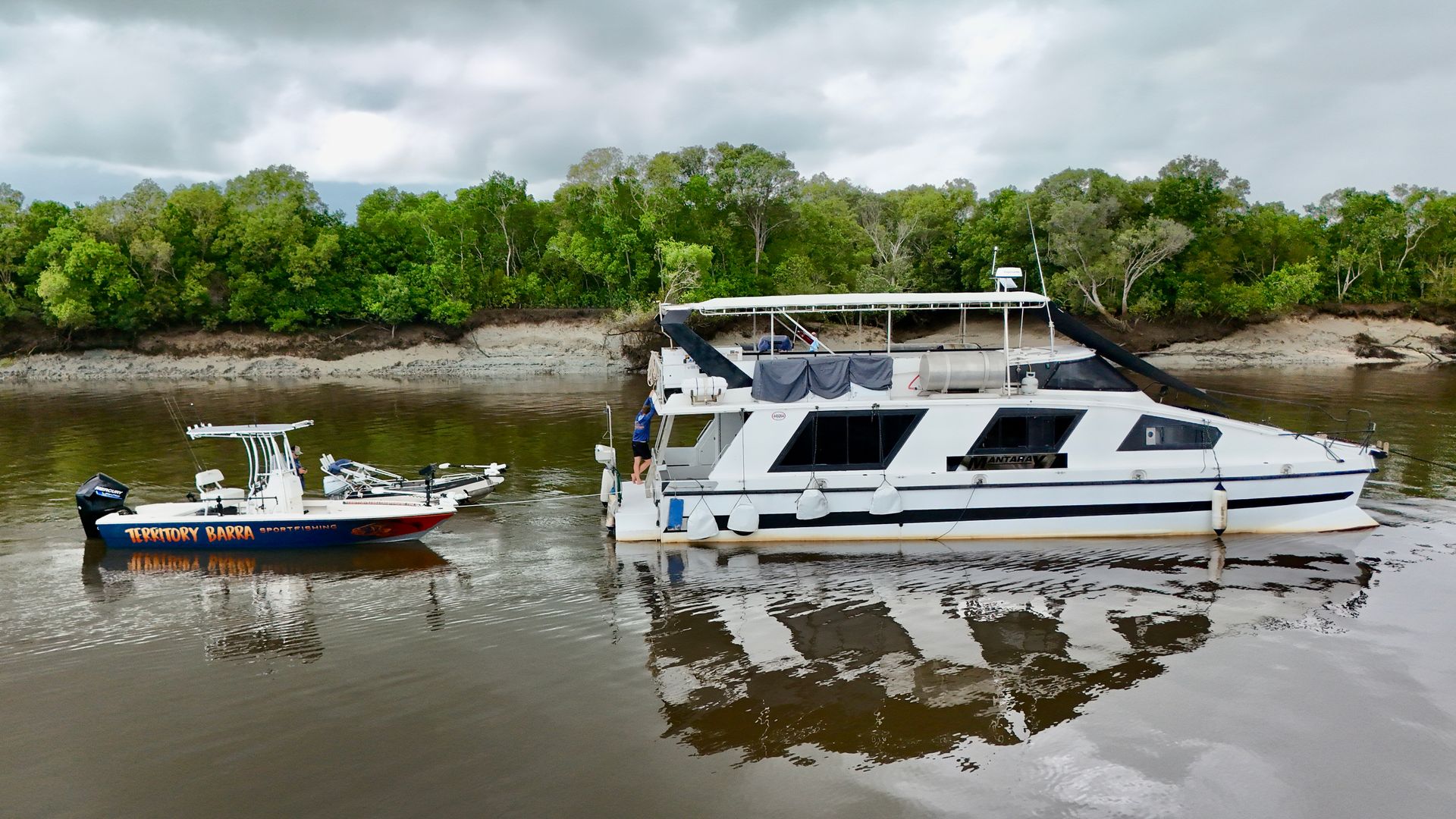 A Man Is Driving A Boat On A Lake With Trees In The Background — Territory Barra Sportfishing In Zuccoli, NT