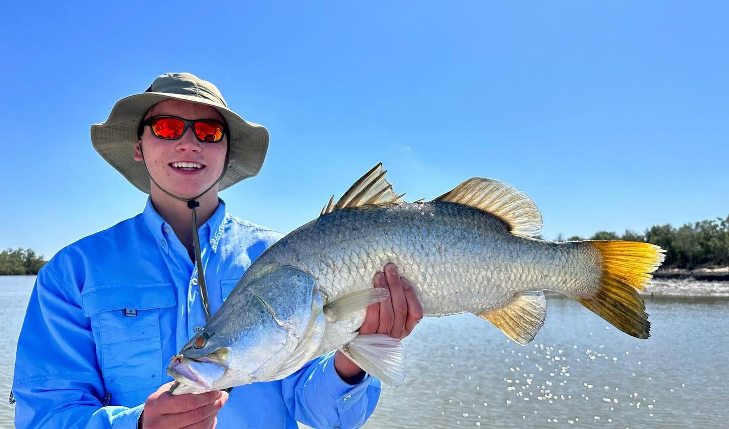 A Man In A Hat And Sunglasses Is Holding A Large Fish In His Hands — Territory Barra Sportfishing In Zuccoli, NT