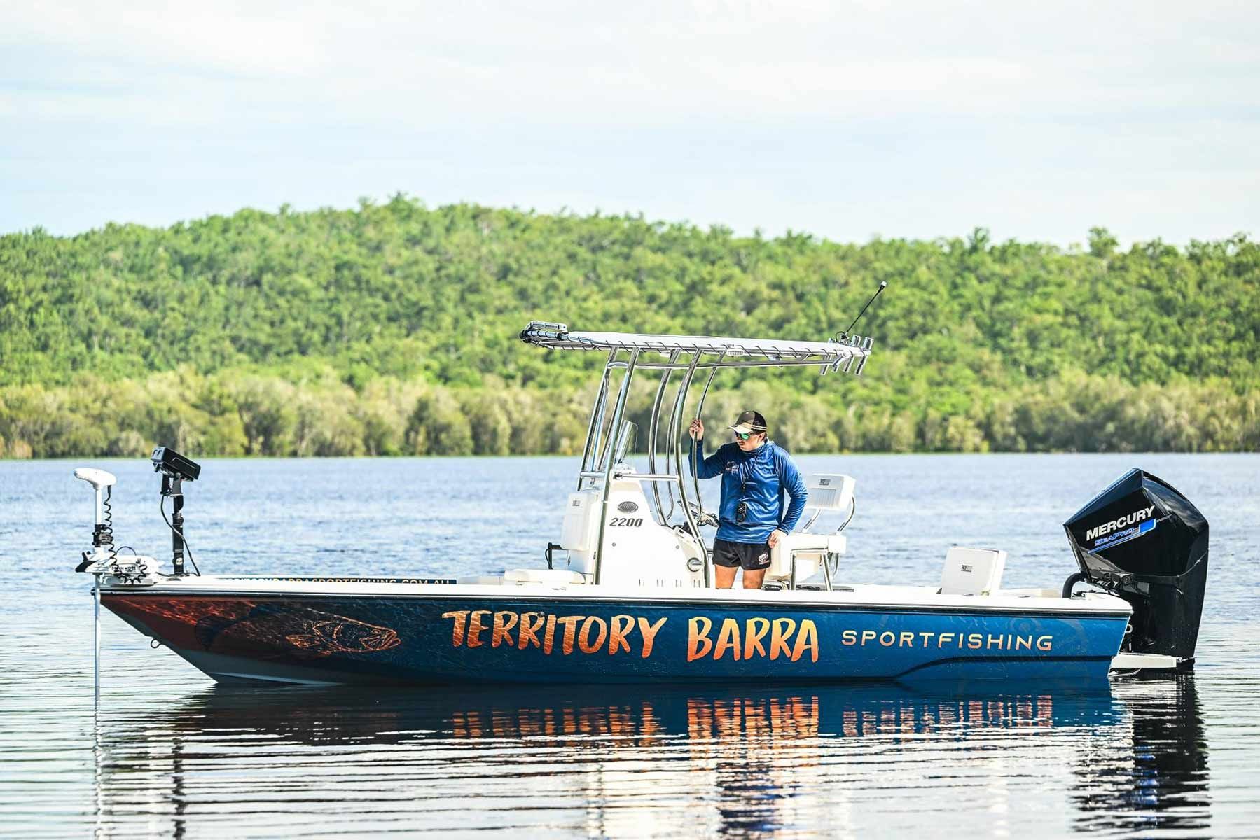 A Man Is Standing On A Boat That Says Territory Barra — Territory Barra Sportfishing In Zuccoli, NT